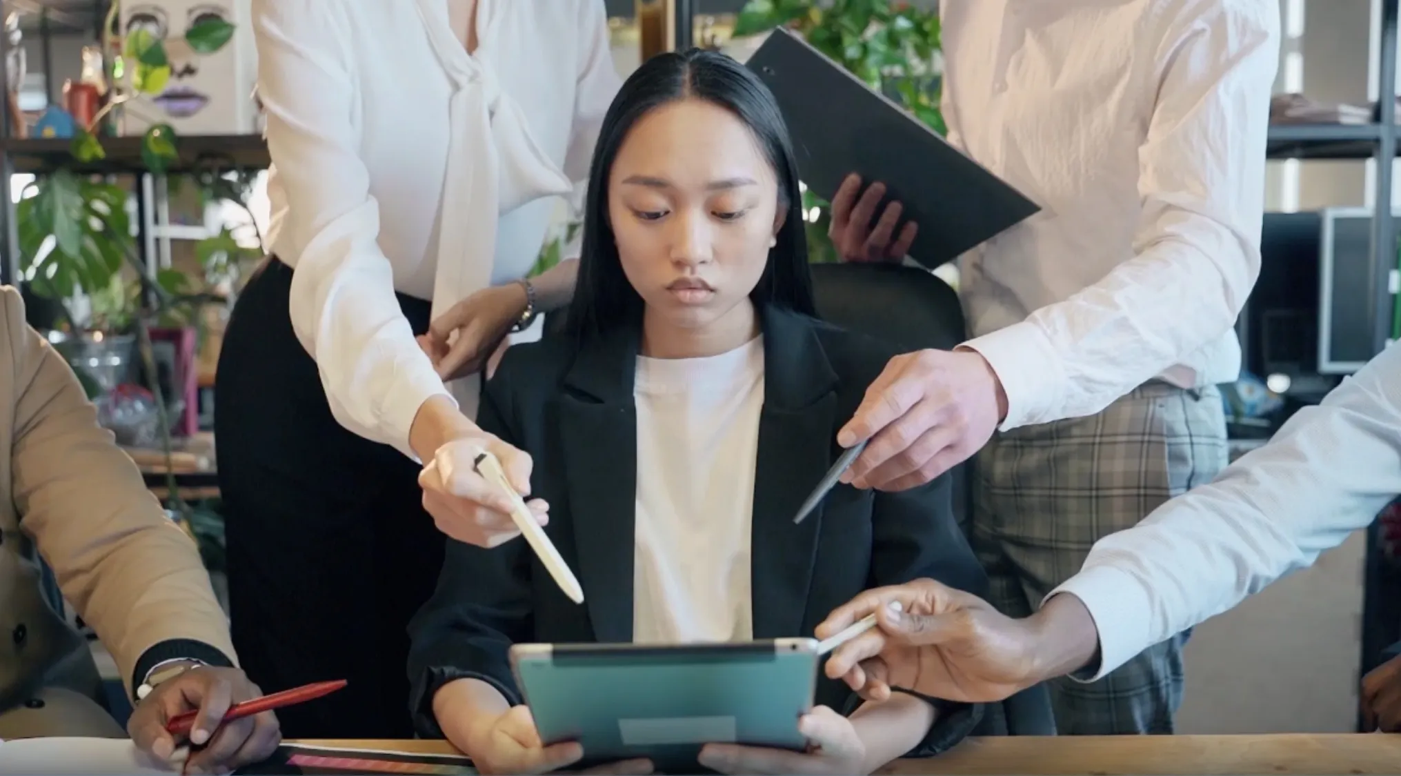 Young woman focused on tablet while colleagues point and discuss geography connection of Canberra, Ottawa, and Brasília.