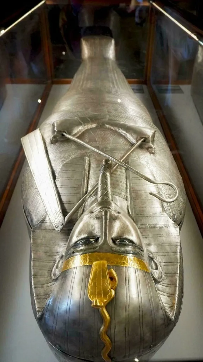 Silver Egyptian mummy case displayed in a museum glass case, showcasing ancient historical finds