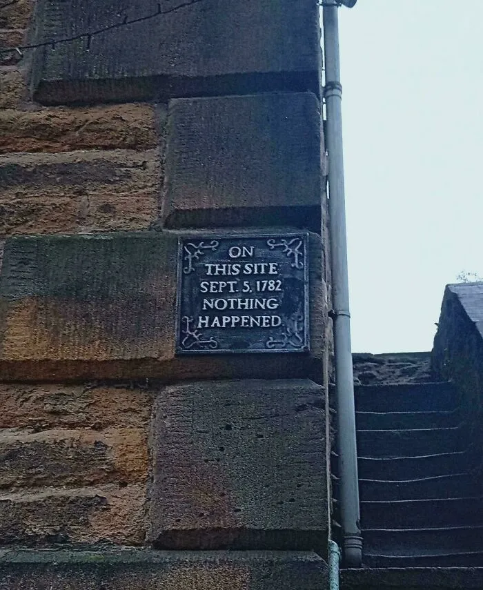 A metal plaque on a stone wall reads On This Site Sept. 5, 1782 Nothing Happened for the Not Interesting community.