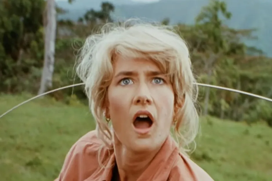 Blonde woman with shocked expression outdoors in a green landscape, related to Jurassic Park character last words question.