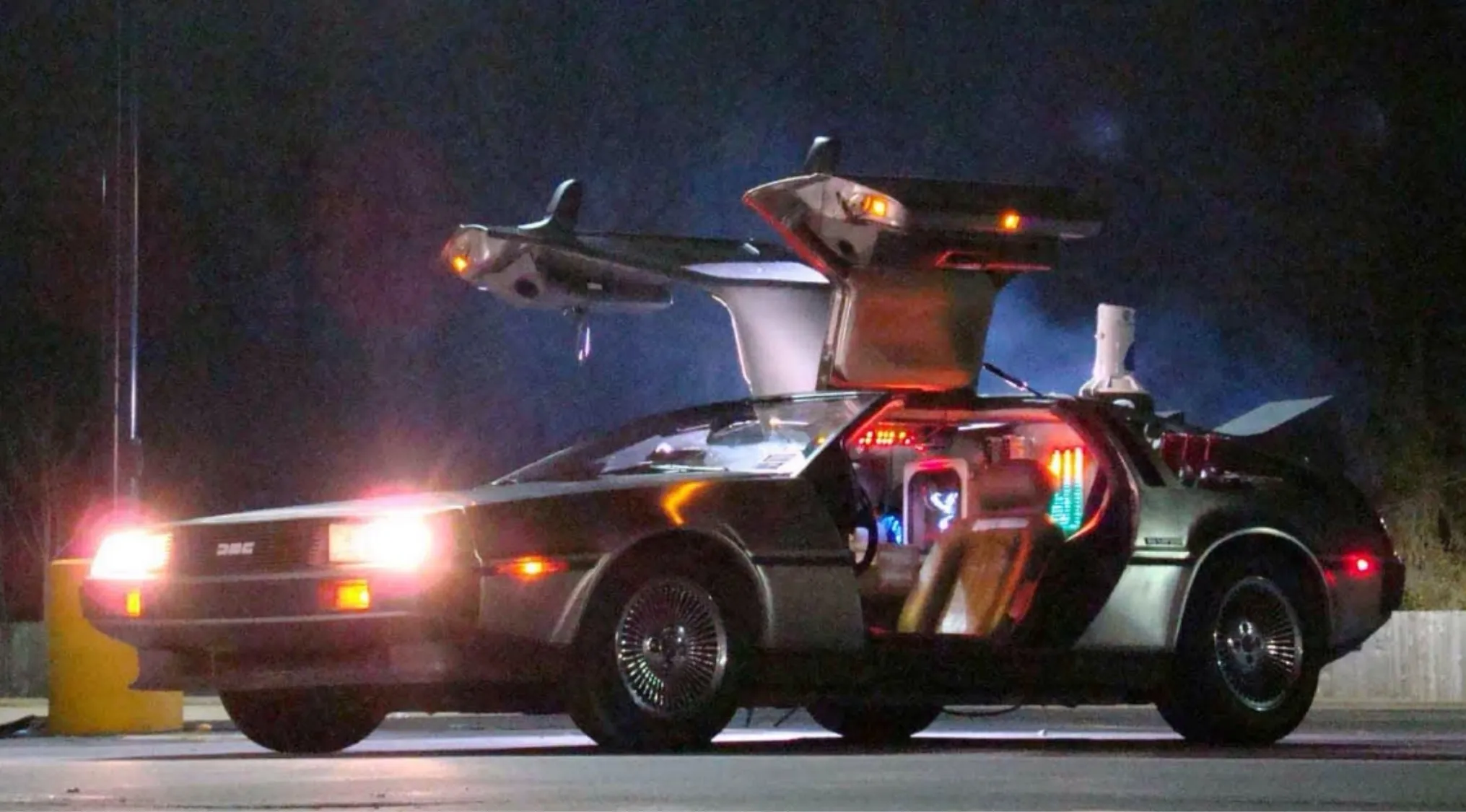 DeLorean time machine with gull-wing doors open at night, featured in '80s pop culture film about time traveling teenager.