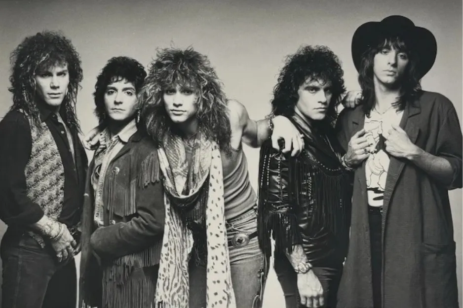 Bon Jovi band members posing in 1980s style clothing with long hair in a vintage black and white promotional photo.