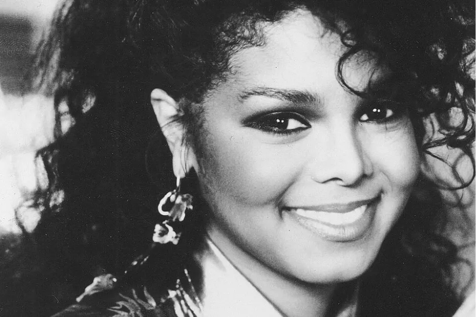Janet Jackson smiling in a vintage black and white photo, known as the Queen of Pop in the 80s.