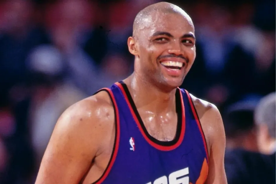 Charles Barkley smiling on the basketball court wearing a Suns jersey during an NBA game in the 1980s.