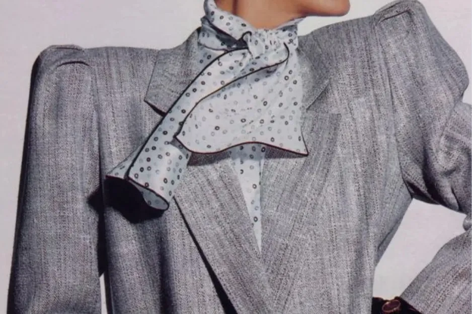 Gray blazer with exaggerated shoulder pads and a patterned scarf, highlighting the 1980s fashion trend of shoulder pads.