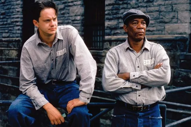 Two men wearing prison uniforms outside a stone building, scene from The Shawshank Redemption movie.