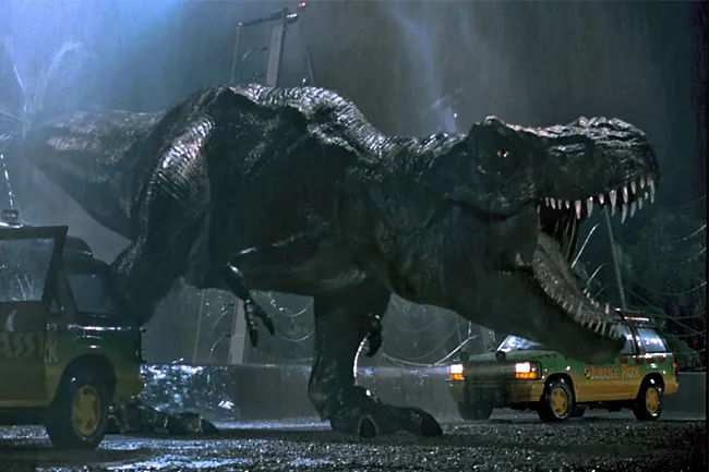 Tyrannosaurus rex roaring at Jurassic Park tour vehicles in a dark, rainy, and suspenseful night scene.