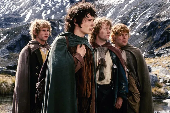 Four hobbits from The Lord of the Rings fellowship standing outdoors in rugged mountainous terrain.