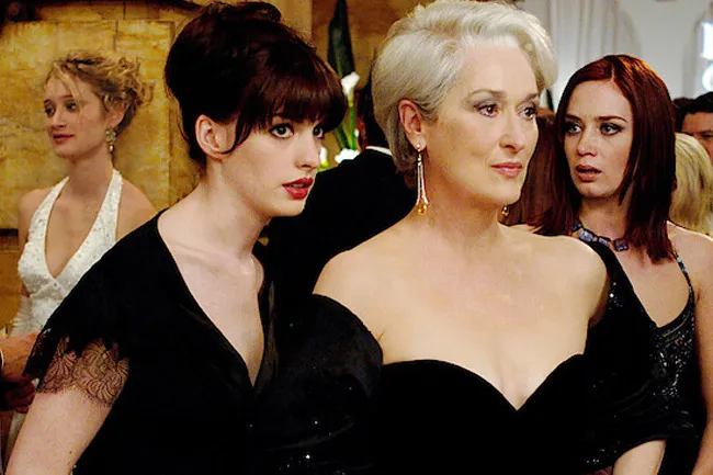 Scene from The Devil Wears Prada featuring three women dressed elegantly at a social event or party.