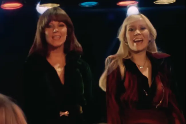 Two women from ABBA singing Dancing Queen, perfect for choosing music for a dinner party playlist.