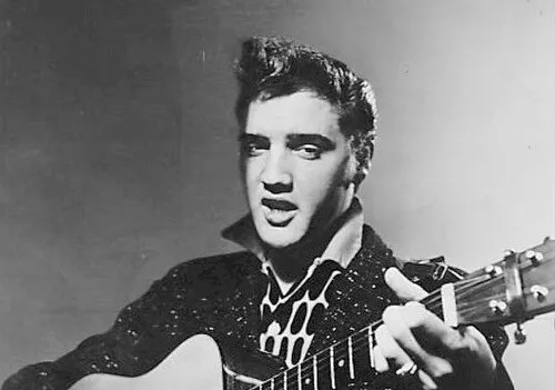 Elvis Presley playing guitar and singing, known as the King of Rock and Roll in a classic black and white photo.