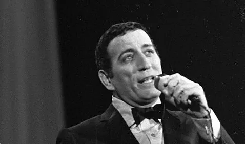 Iconic crooner performing live in a black suit and bow tie, holding a microphone during a classic 1950s music event.