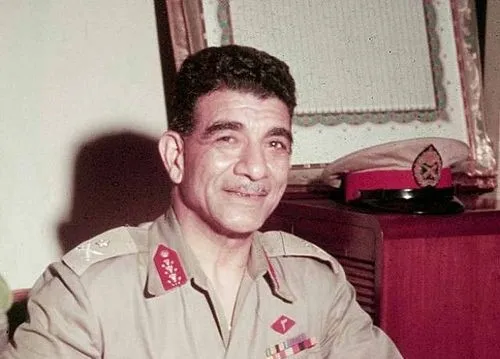 Muhammad Naguib in military uniform sitting near desk with Suez Canal nationalization historical context.