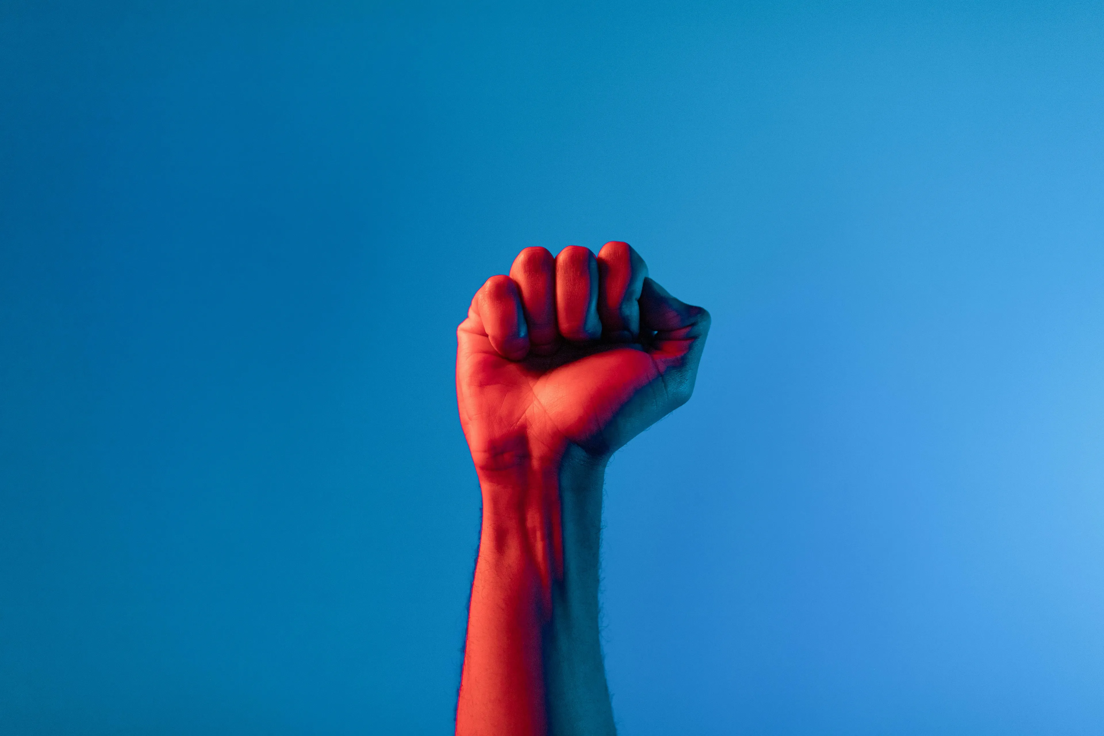 Raised fist symbolizing African independence and empowerment with blue background in a dramatic red light.