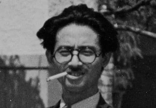 Black and white photo of iconic Japanese film director wearing glasses and smoking a cigarette outdoors.