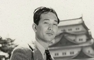 Akira Kurosawa, iconic Japanese film director, posing outdoors in front of traditional architecture, black and white photograph.