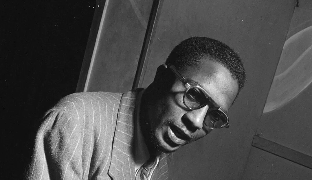 Legendary jazz musician Thelonious Monk wearing glasses and a striped suit, captured in a black and white portrait.