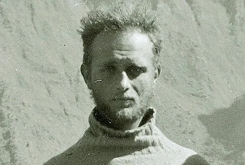 Black and white photo of a New Zealand mountaineer wearing a high-collar sweater with a mountainous background.