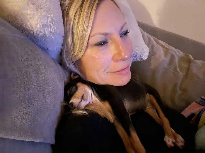 Woman resting on a couch with a small dog sleeping on her chest, showing animals saved from awful conditions.