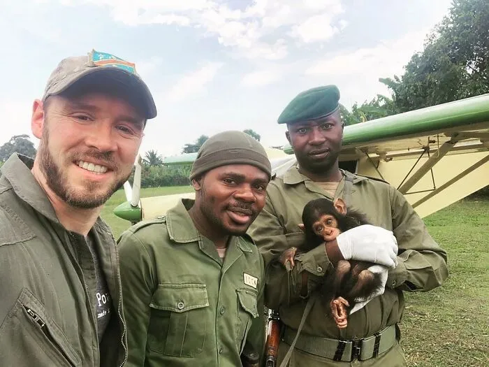 Three rescuers smiling outdoors with a baby chimpanzee rescued from awful conditions, giving it a second chance in life.