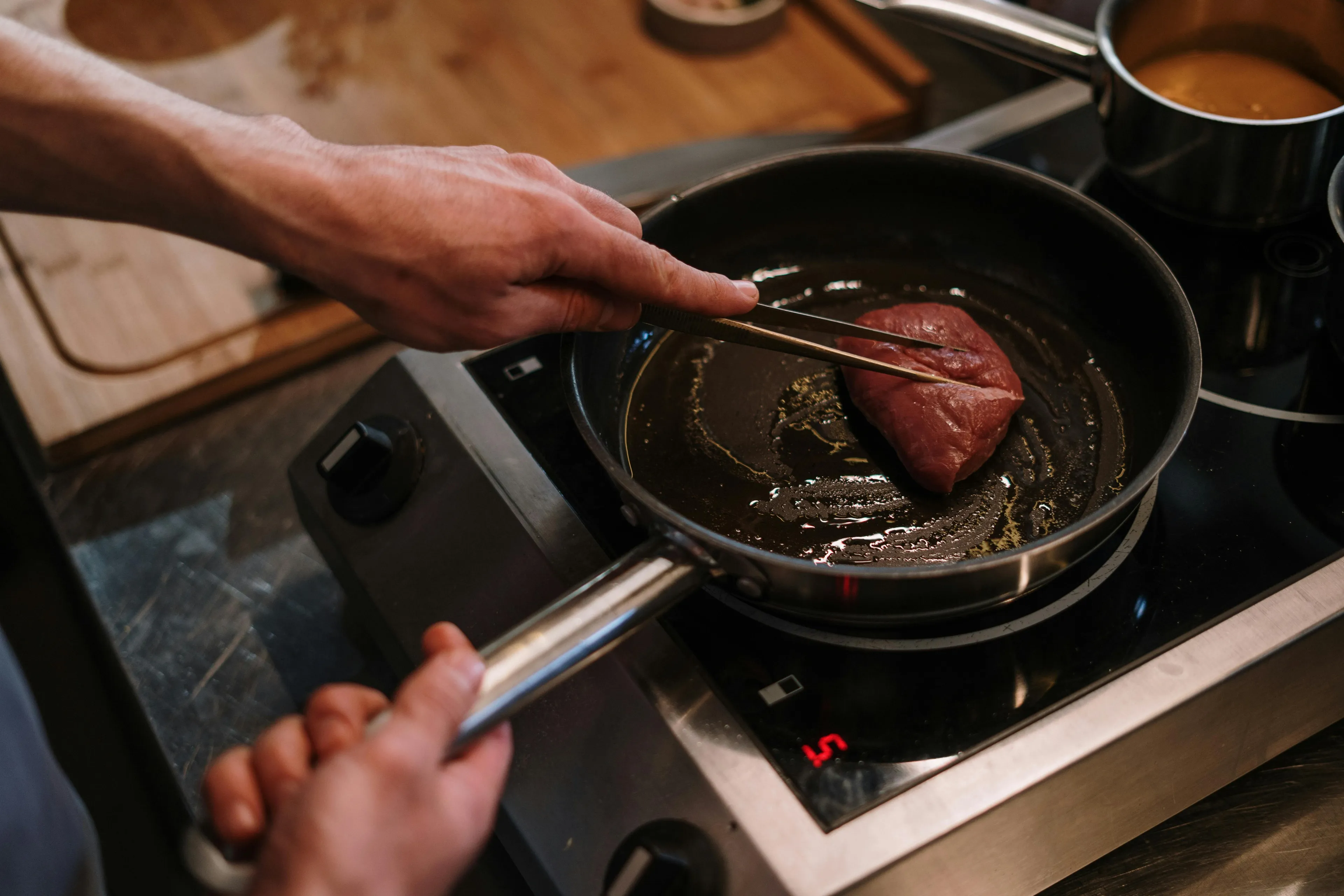 Person cooking a piece of meat in a frying pan using chopsticks on a stovetop, enjoying the hobby of cooking.