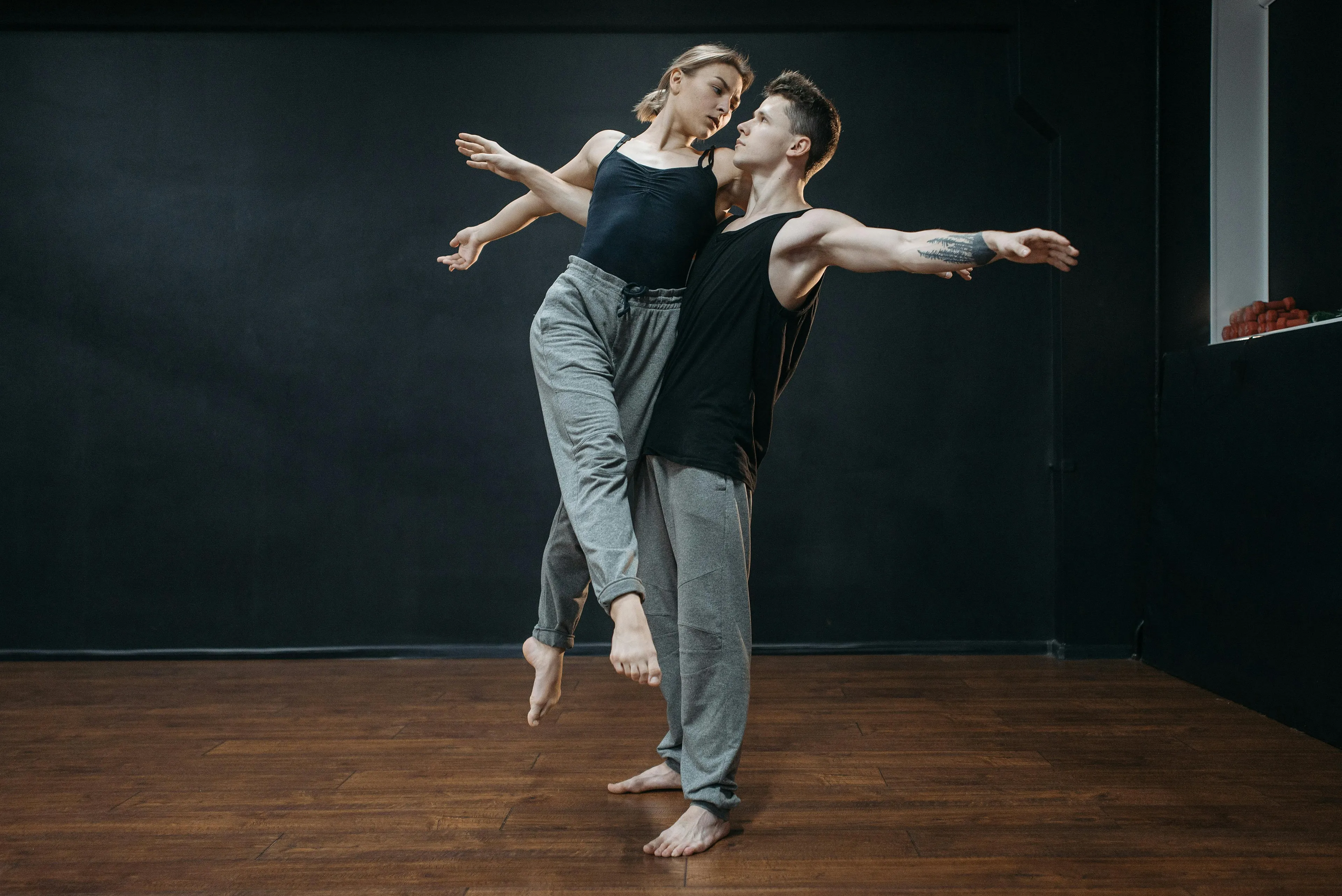 A young couple practicing contemporary dancing in a studio with wooden floors and a dark background.