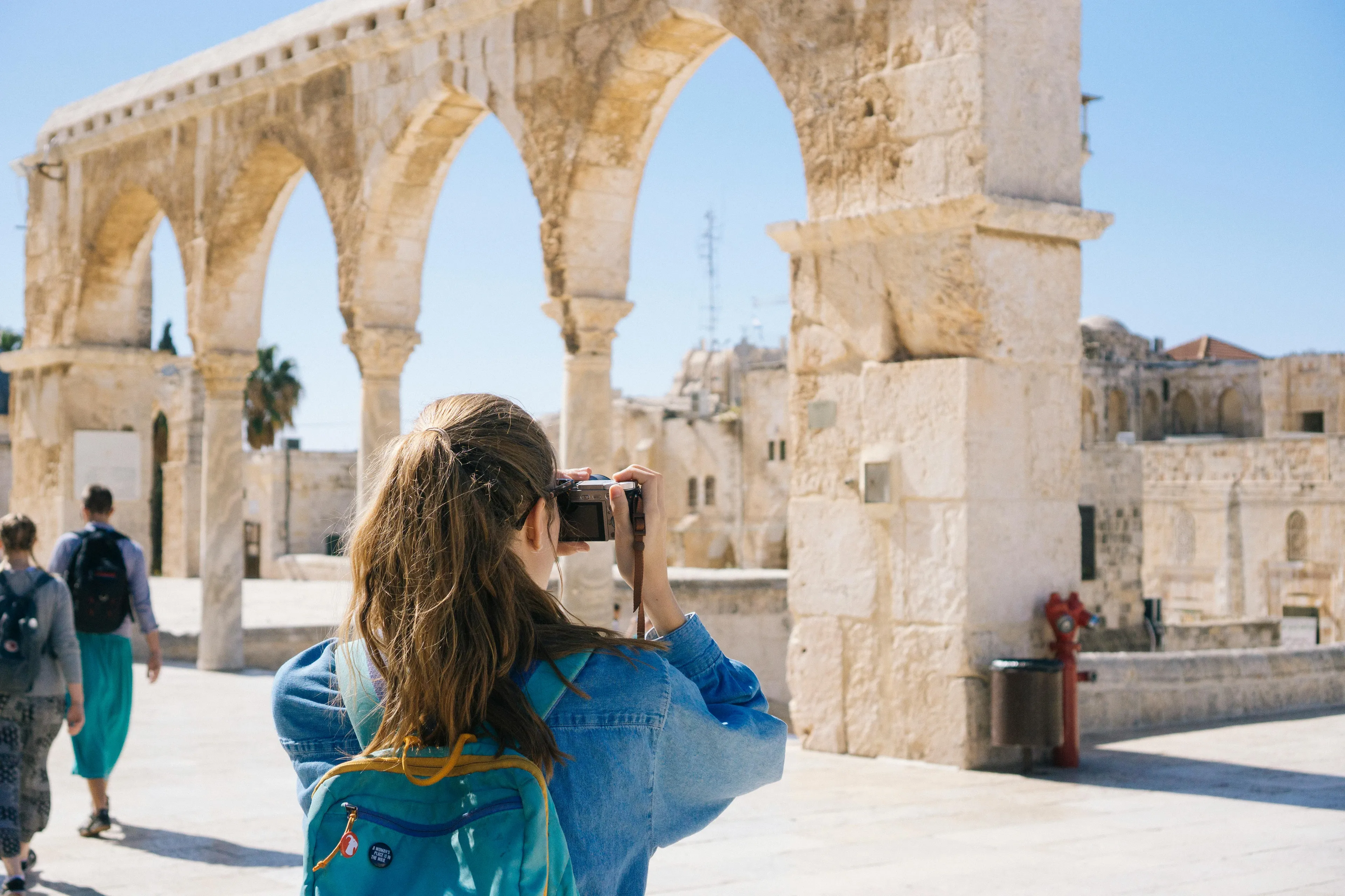 Traveler with a backpack taking photos of ancient stone arches at a sunny historical site, enjoying the traveling hobby.