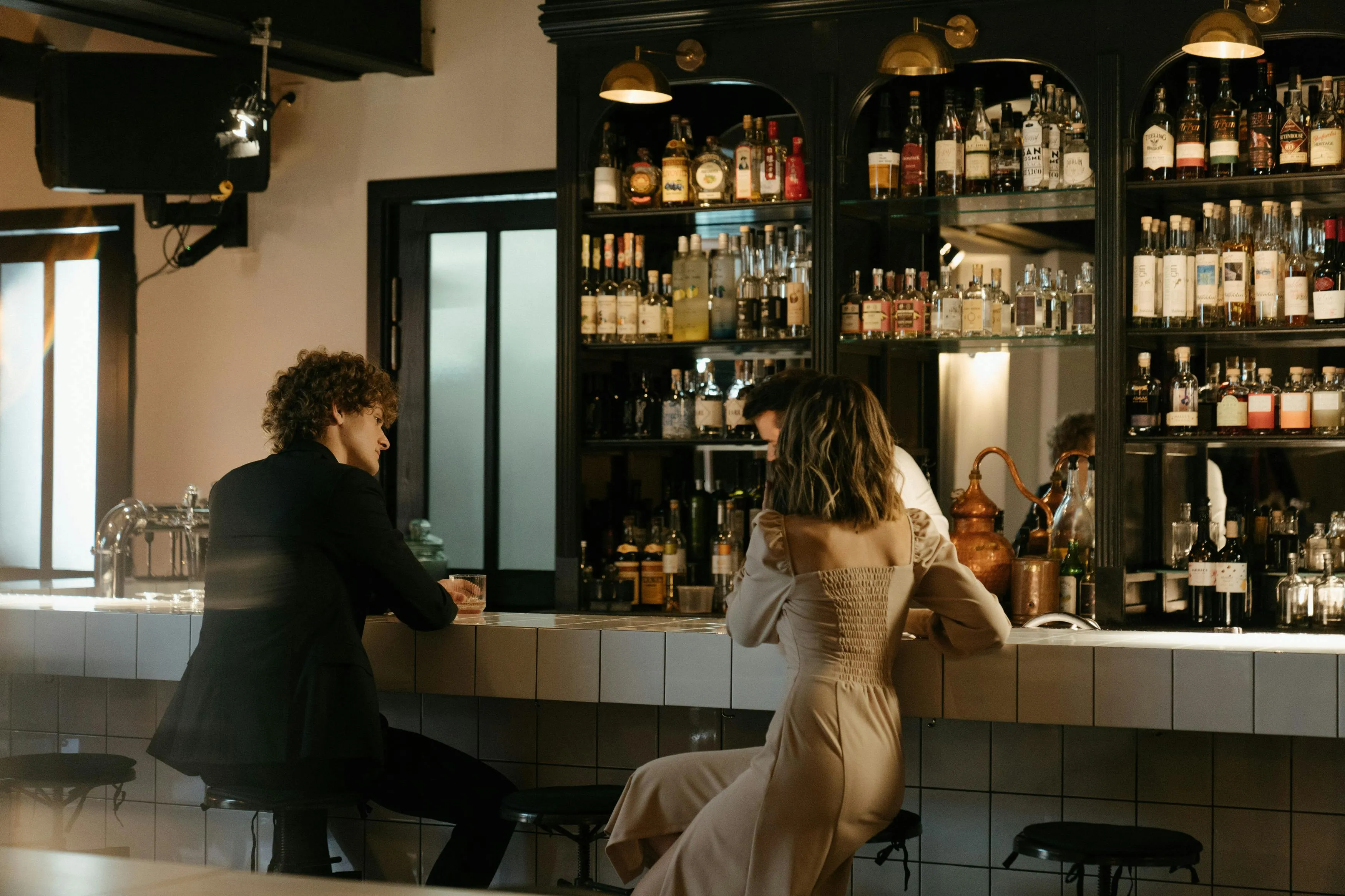 Two friends sitting at a bar counter, chatting and enjoying drinks in a cozy, stylish going out to a bar setting.