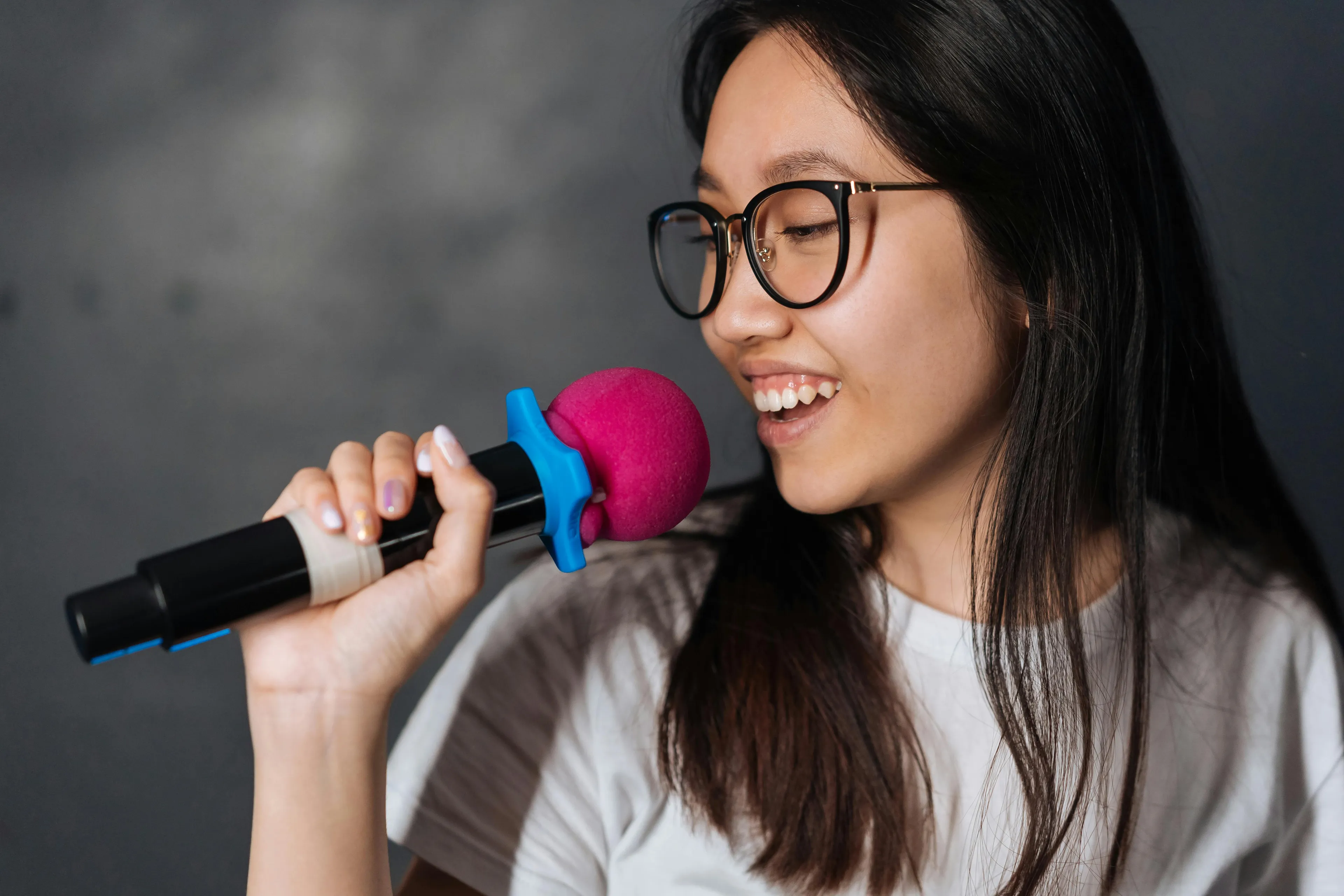 Young woman with glasses holding a microphone and singing happily during a karaoke night event.