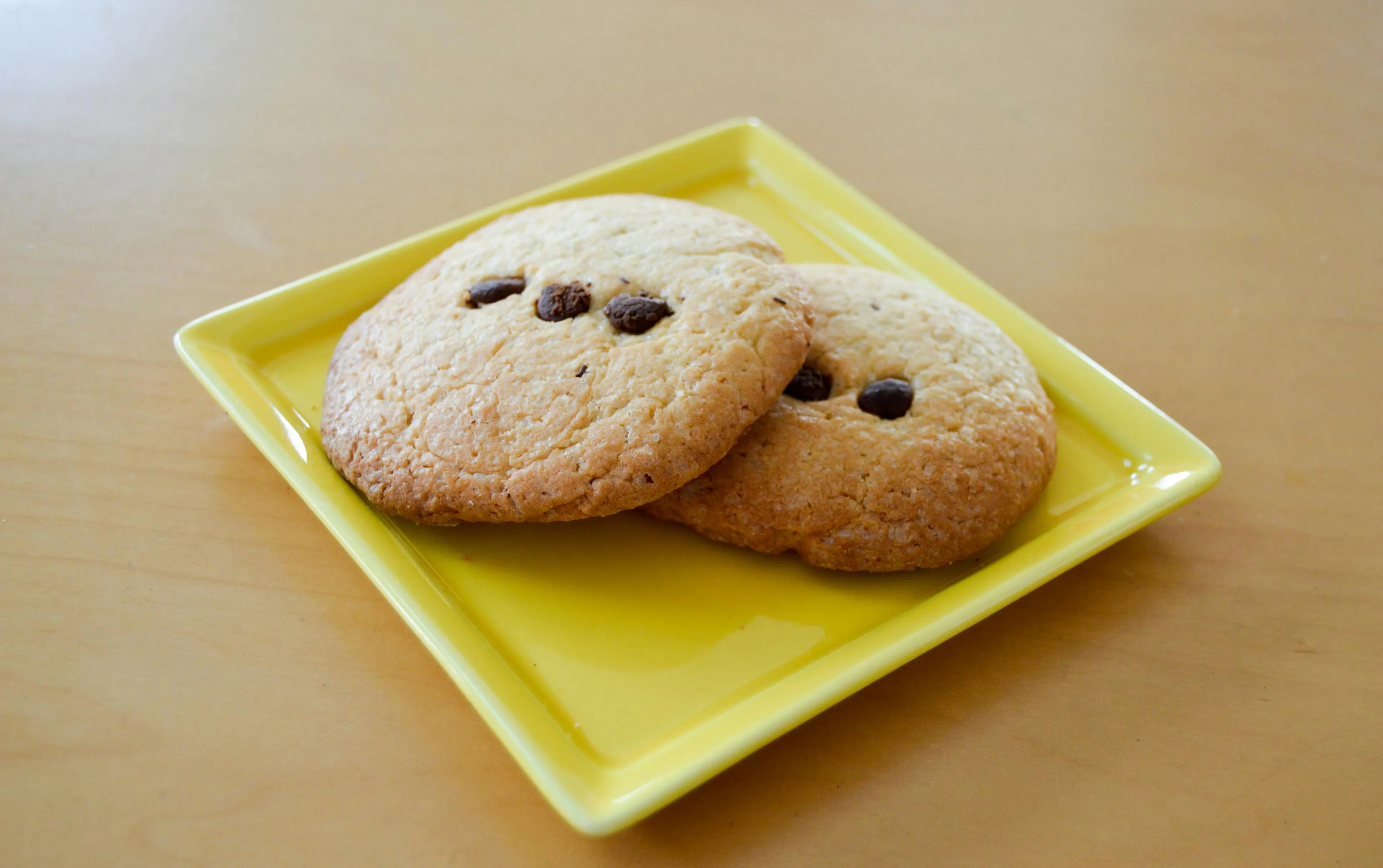 Two chocolate chip cookies on a yellow plate in an office kitchen, testing your ability to control your urges.