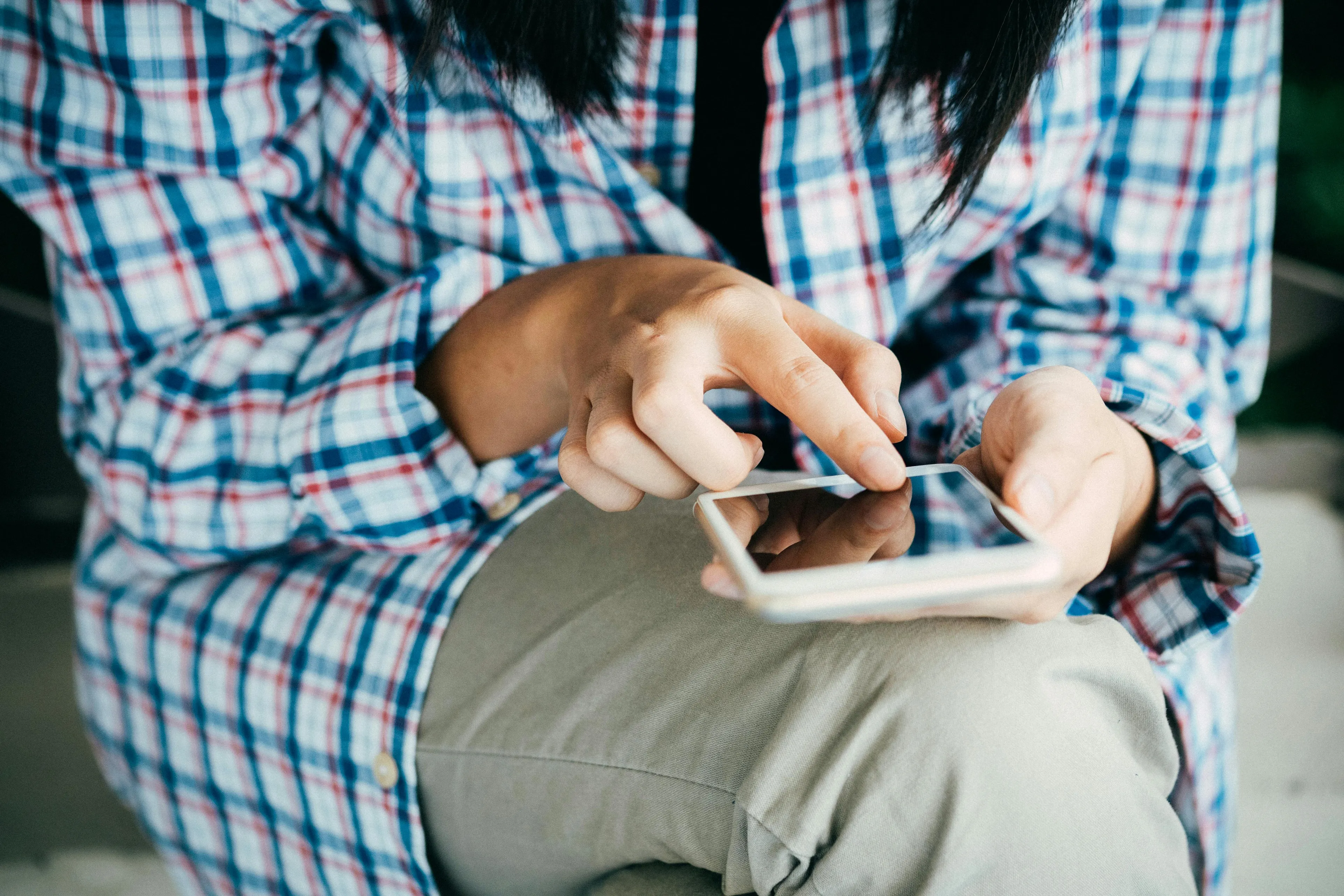 Person in a plaid shirt controlling urges while texting on smartphone, deciding between binge-watching and planned chores.