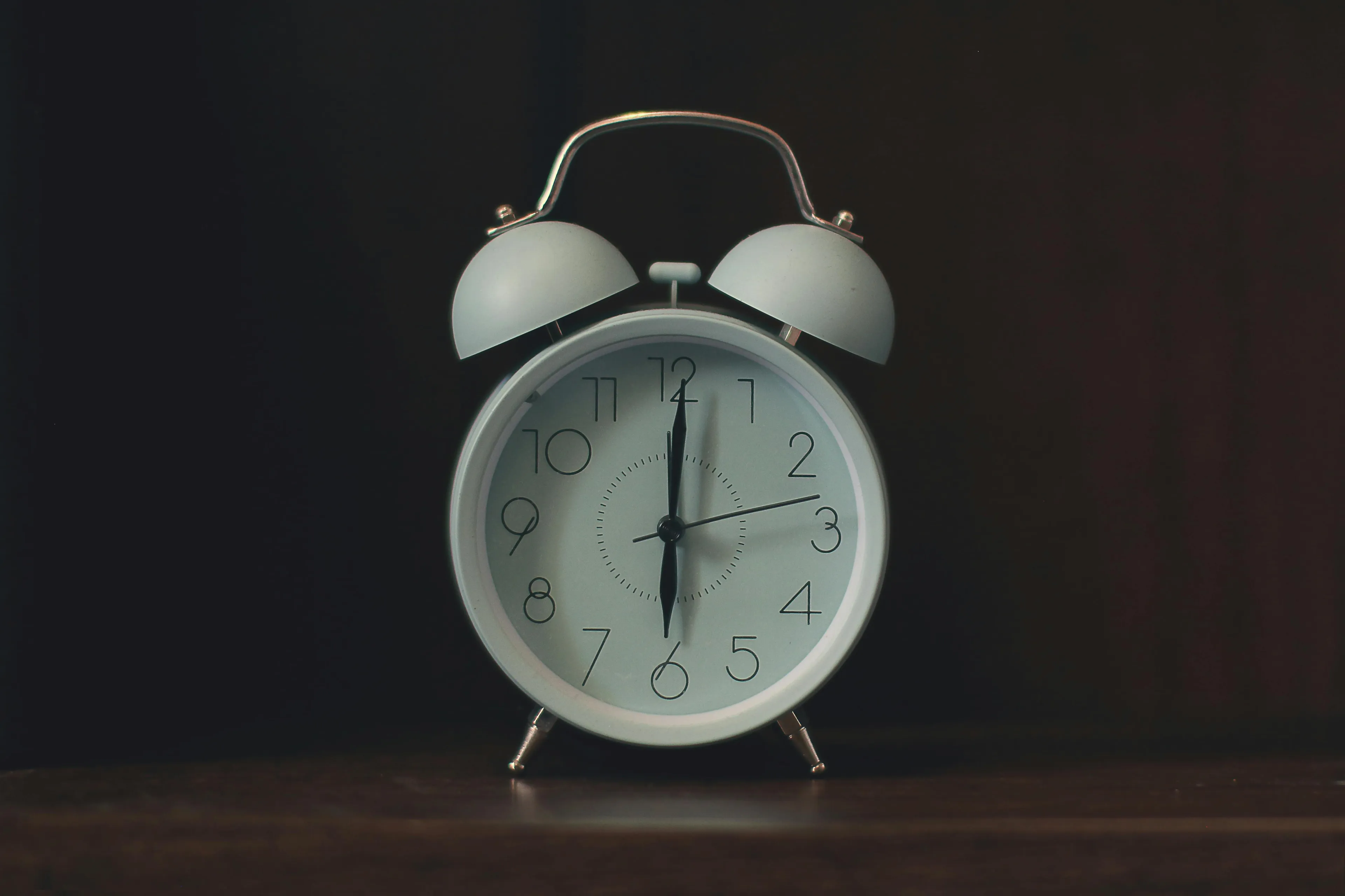 White alarm clock showing 6 a.m. in a dark room, symbolizing the challenge to control your urges early on a cold Saturday.