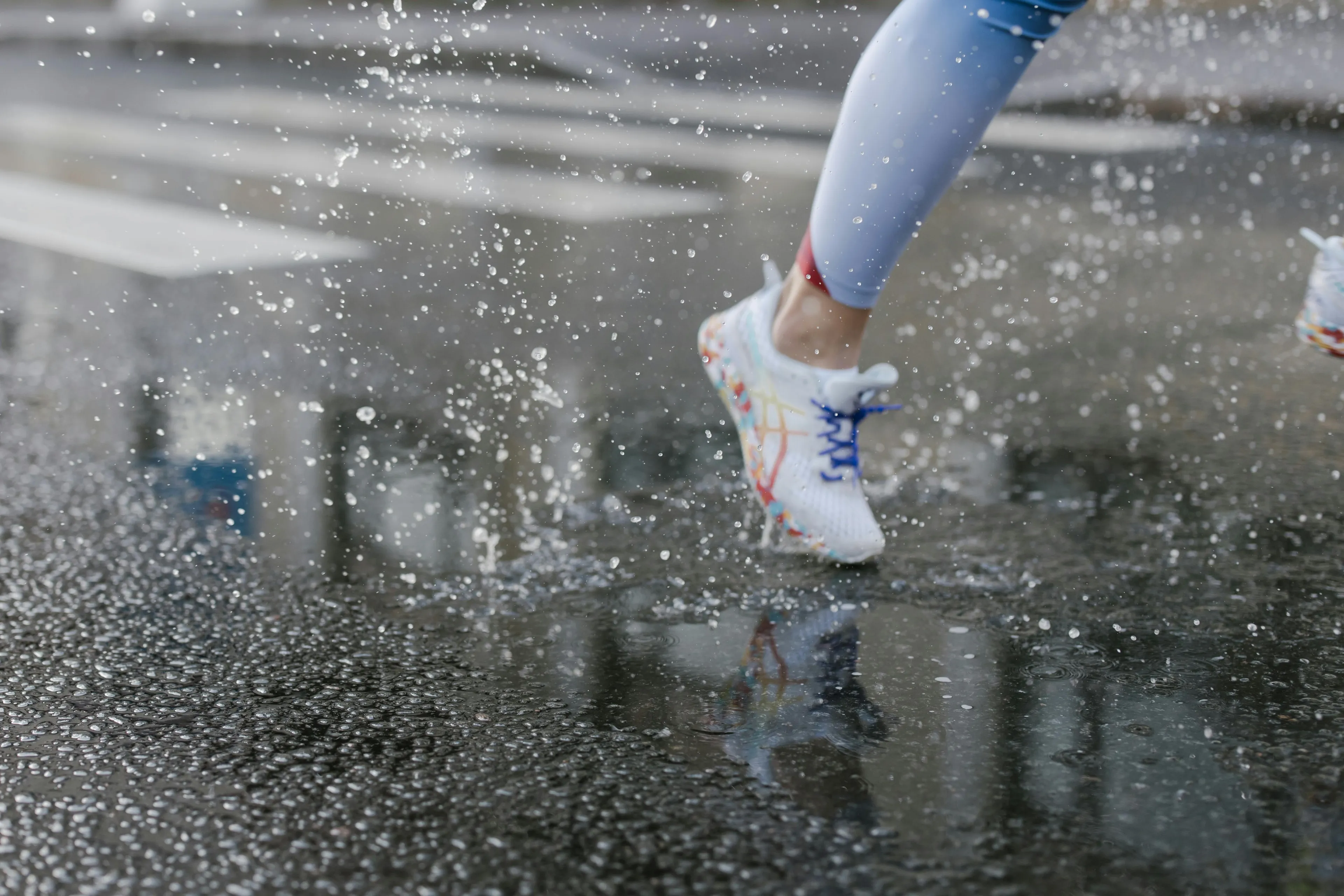 Runner in colorful shoes splashing water on wet pavement during rain, illustrating control over urges while jogging.