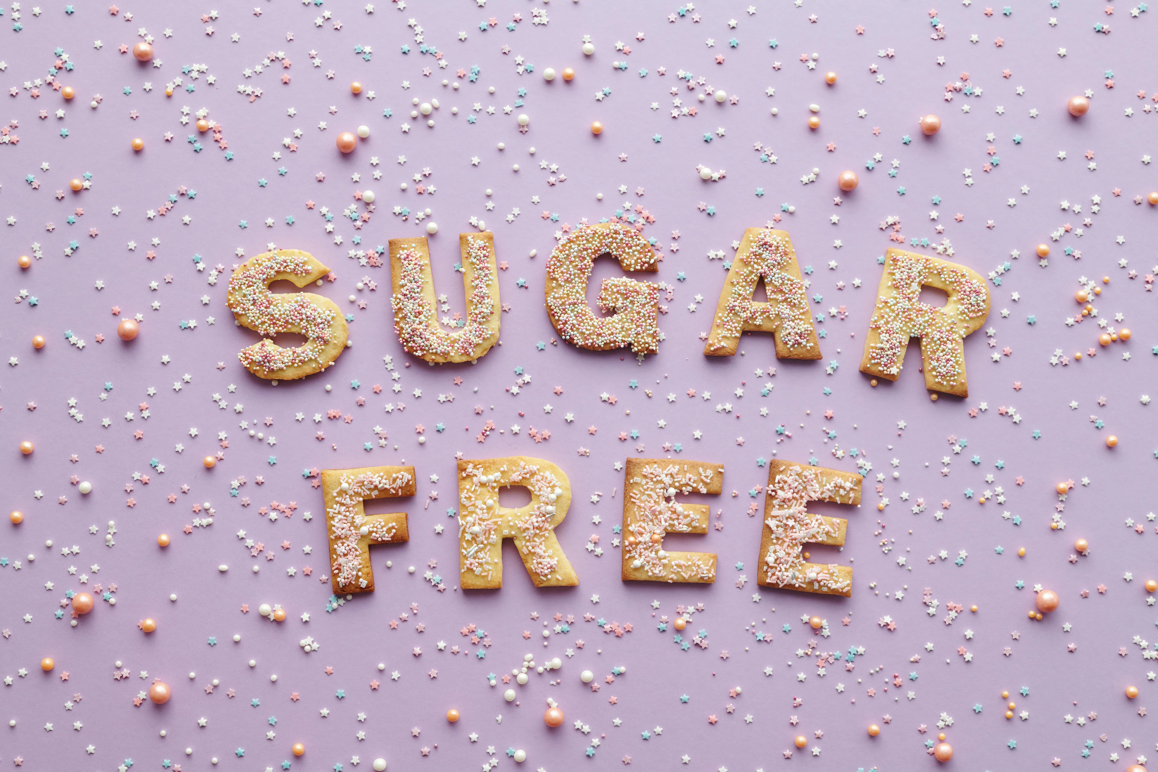 Cookies shaped as letters spelling sugar free with sprinkles on a purple background representing controlling urges for added sugar.