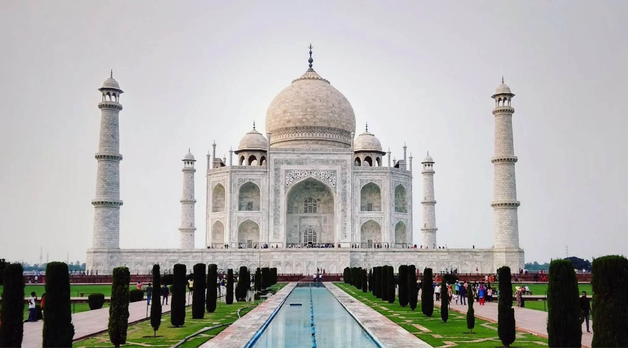 Taj Mahal in India with minarets and reflection pool surrounded by visitors and gardens under a clear sky