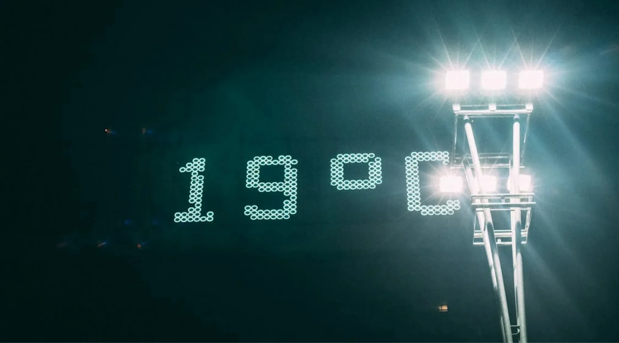 Digital display showing temperature as 19 degrees Celsius next to a bright stadium light tower at night