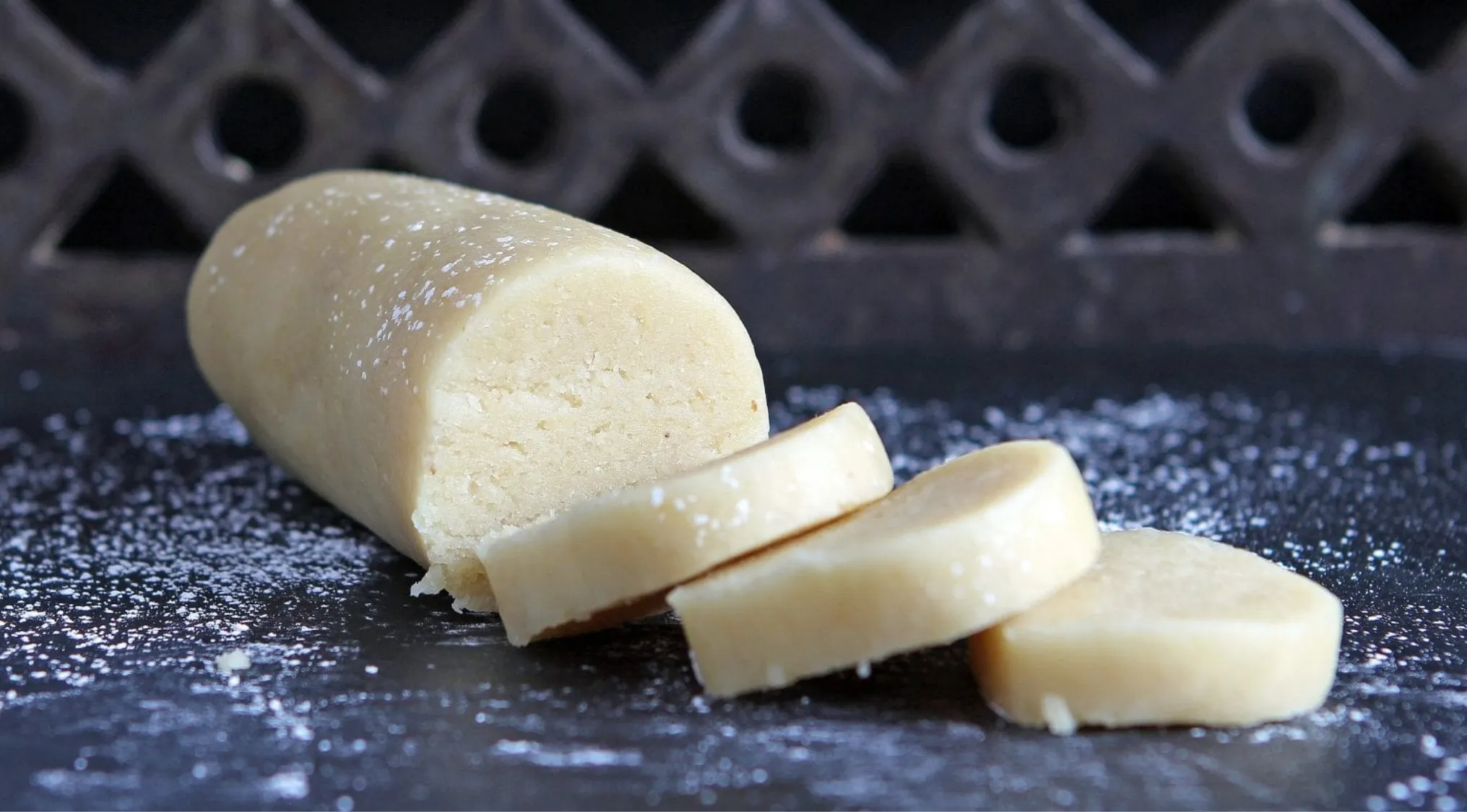 Marzipan log and slices on a dark surface dusted with powdered sugar, made from almonds nut.