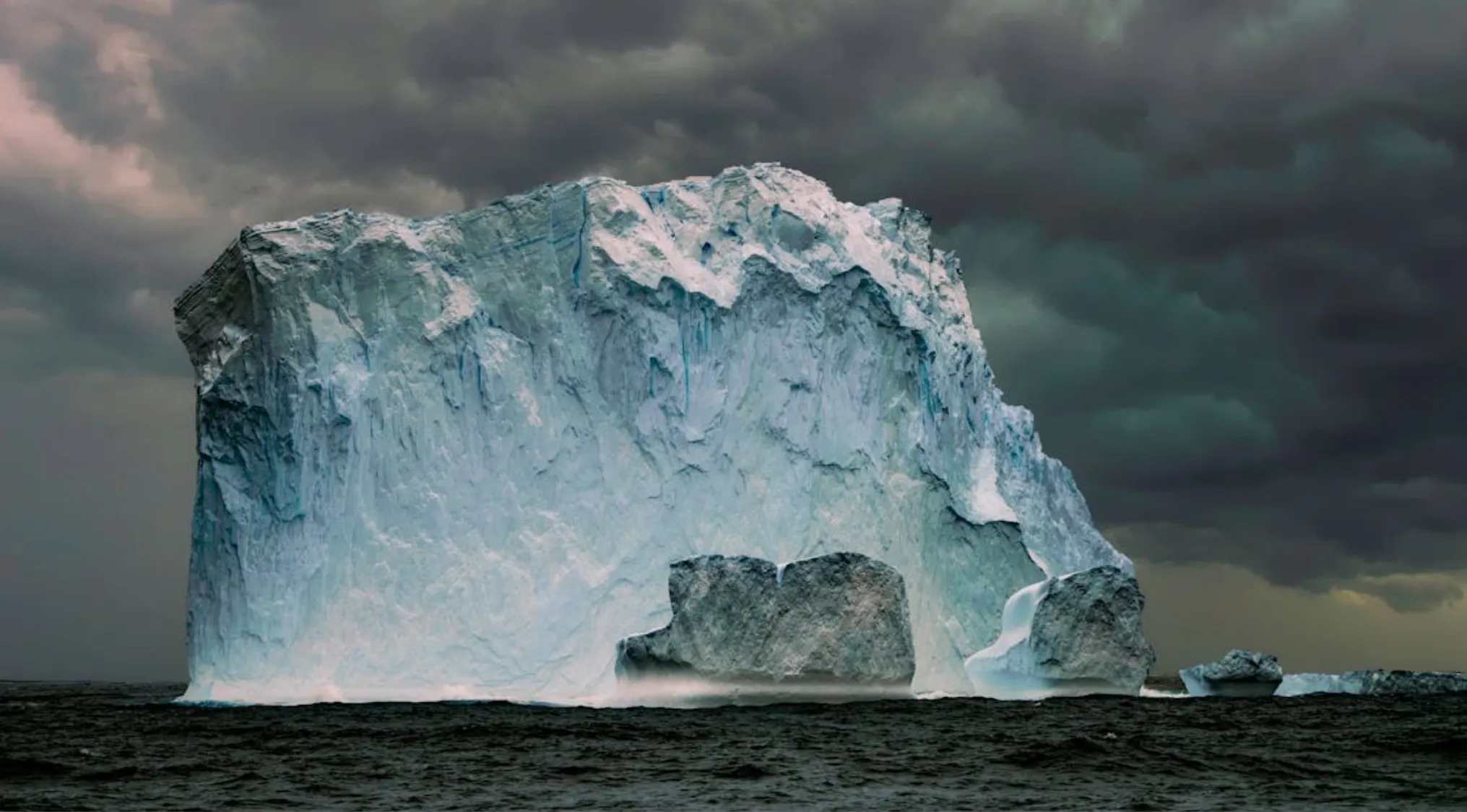 Large iceberg floating in dark ocean waters under a stormy sky related to famous ship sinking in 1912.