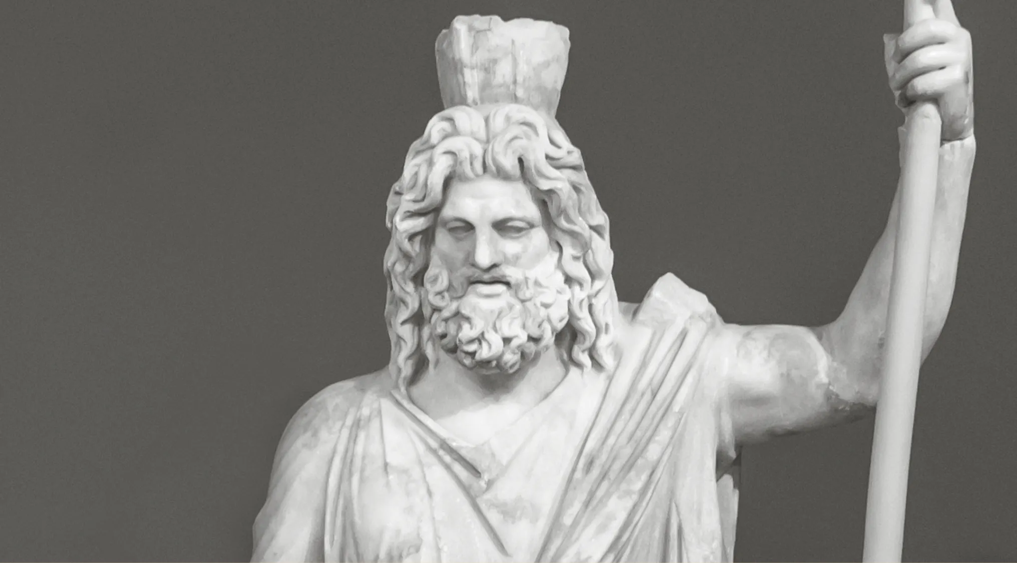 Marble statue of a Greek god holding a staff, representing the Greek god of the underworld in ancient mythology.