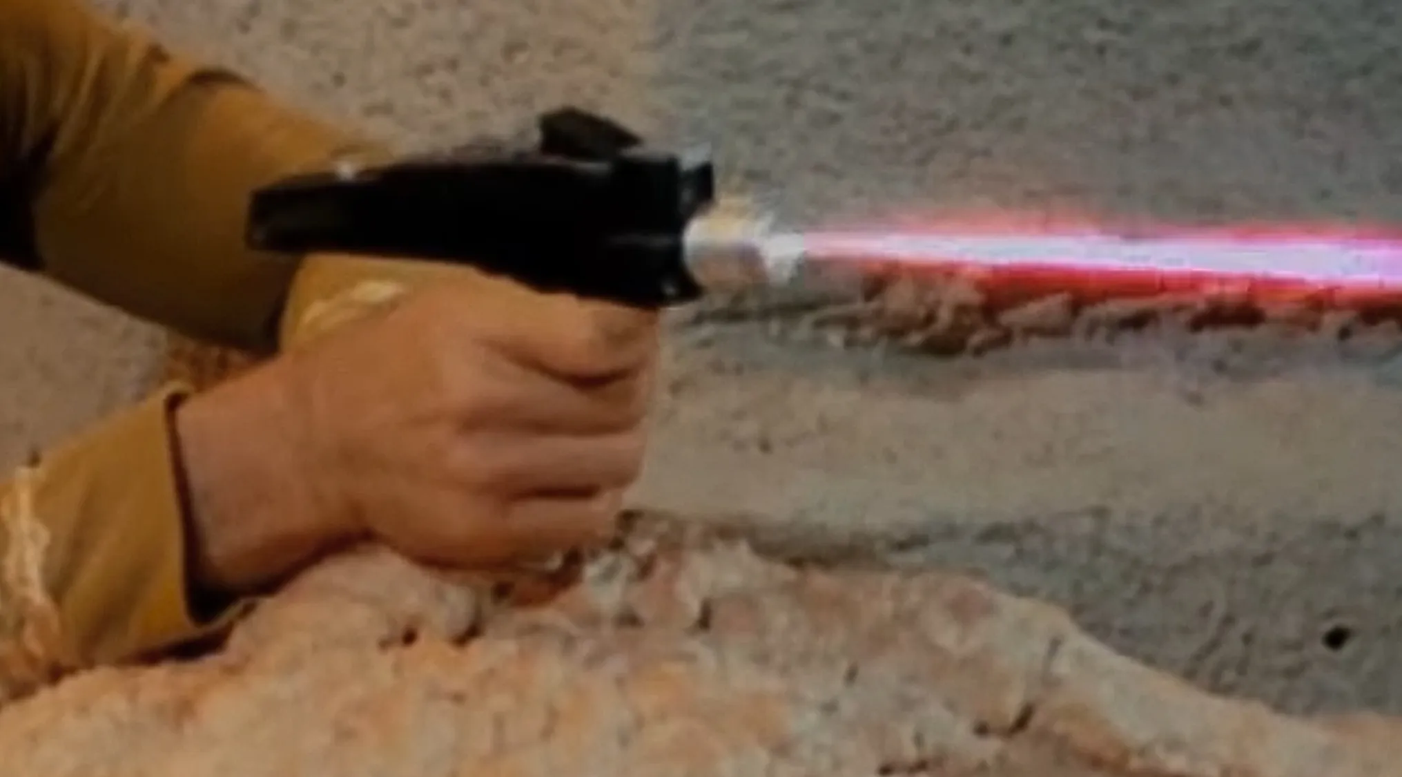 Hand holding a multi-purpose prop firing a red beam in a TV show props quiz scene.