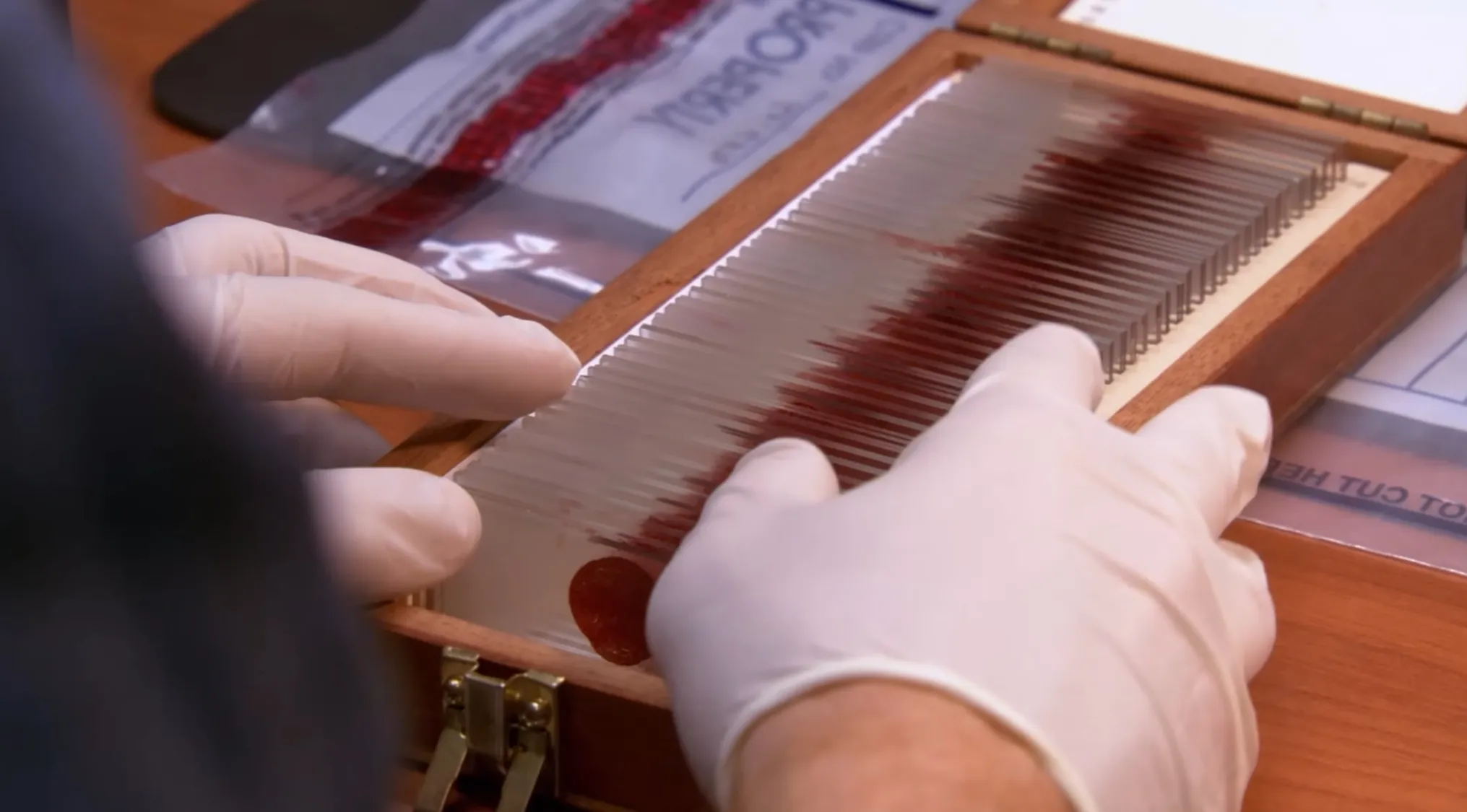 Hands wearing white gloves examining a wooden box with glass slides in a TV show props quiz setup.