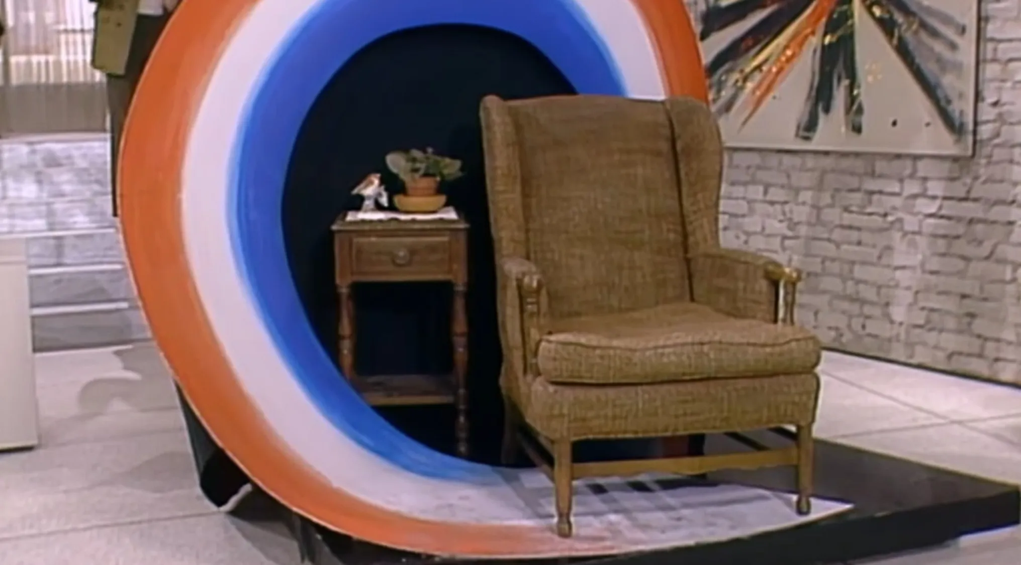 Vintage brown armchair and wooden side table inside circular set piece from a TV show props quiz scene.