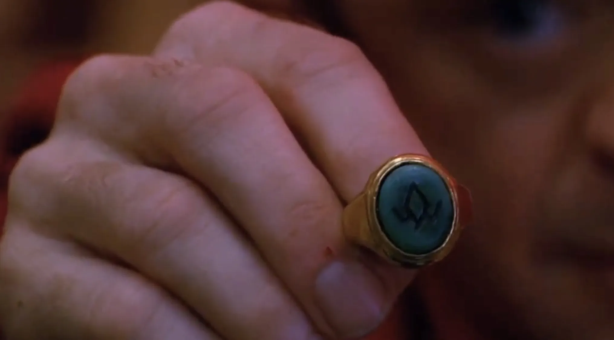 Close-up of a hand wearing a gold ring with a blue stone featuring a black symbol from TV show props quiz accessory.