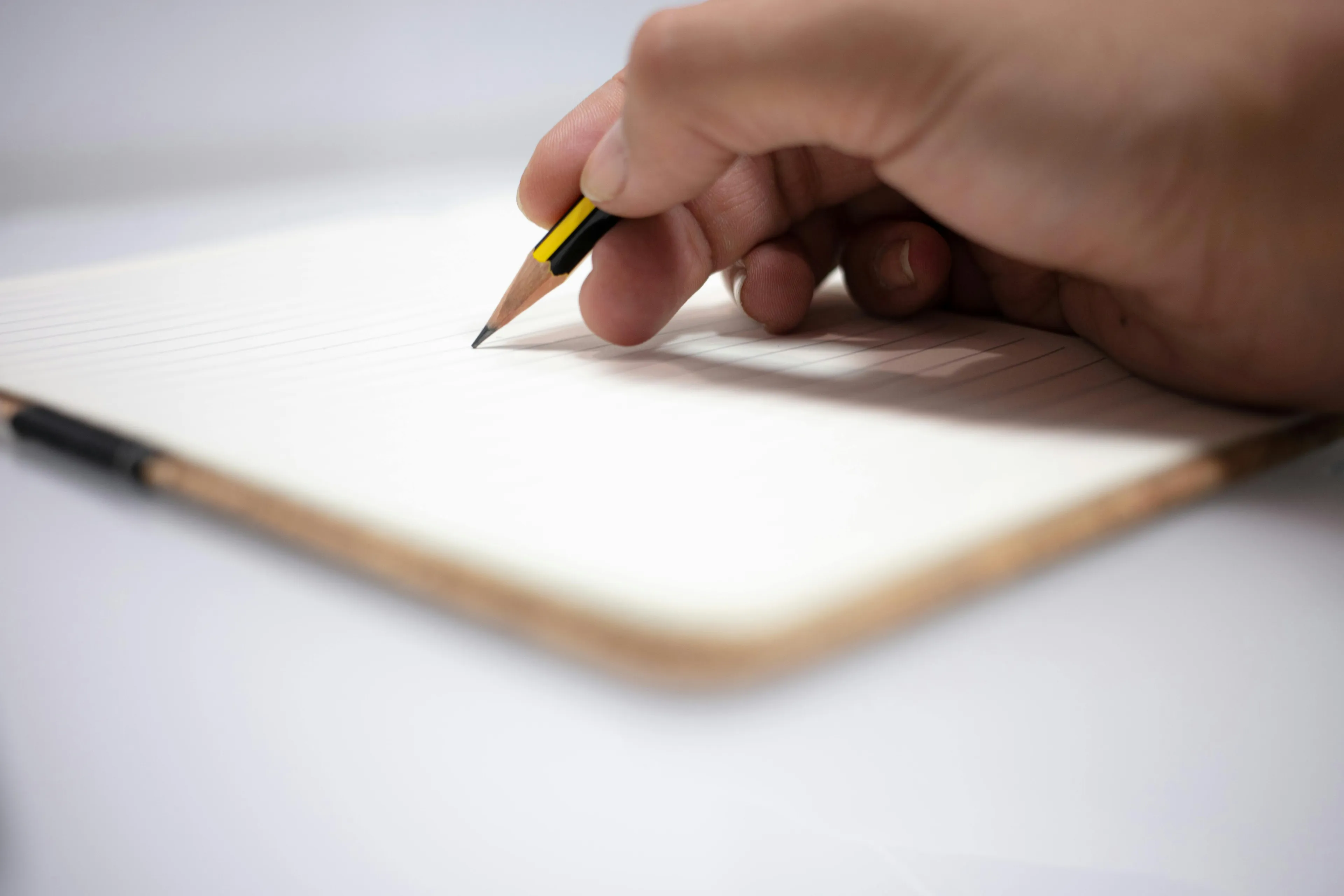 Hand holding pencil poised to write on lined notebook, illustrating advanced placement school quiz English language concept.