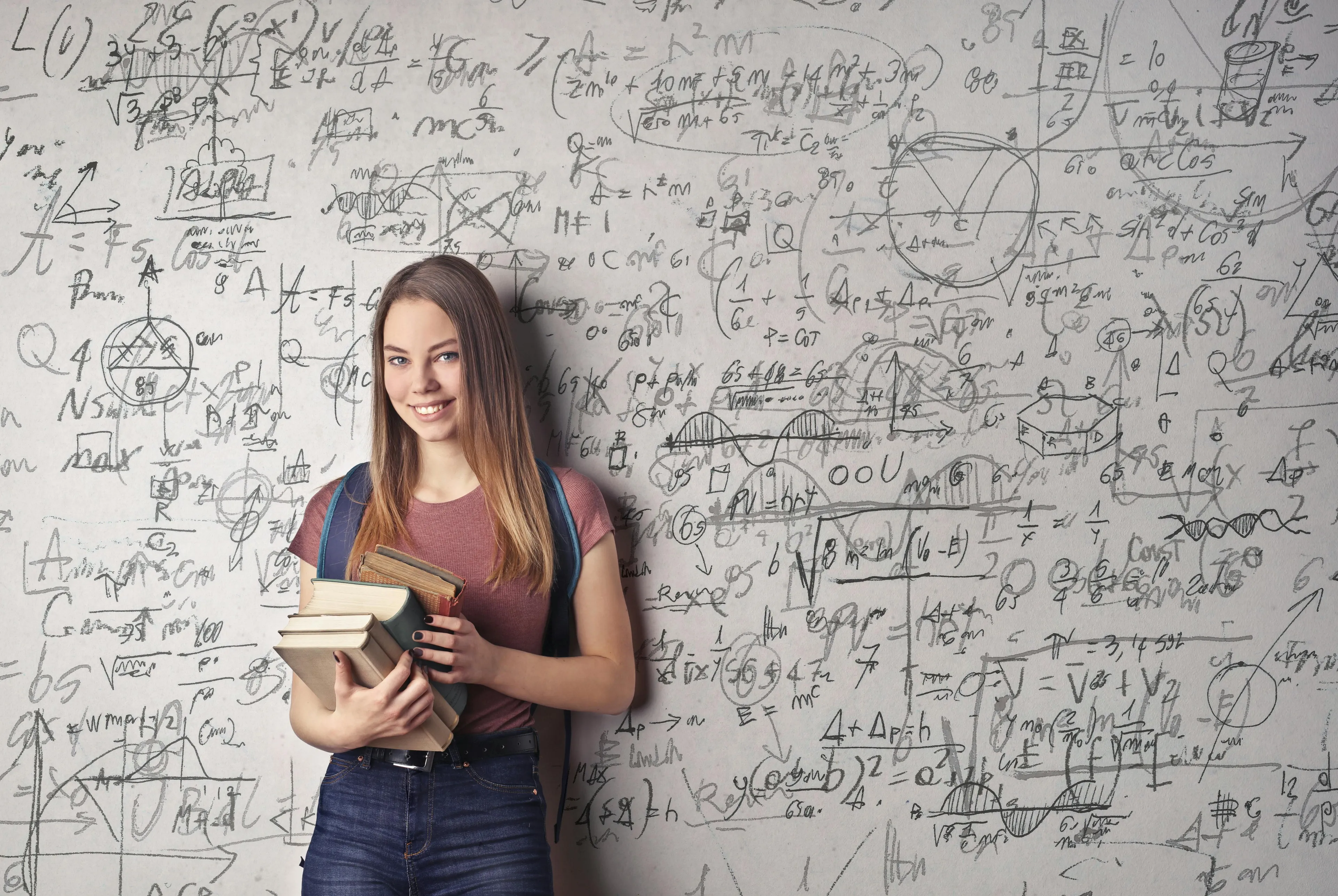 Female student holding books standing in front of chalkboard filled with advanced placement school quiz statistics formulas.