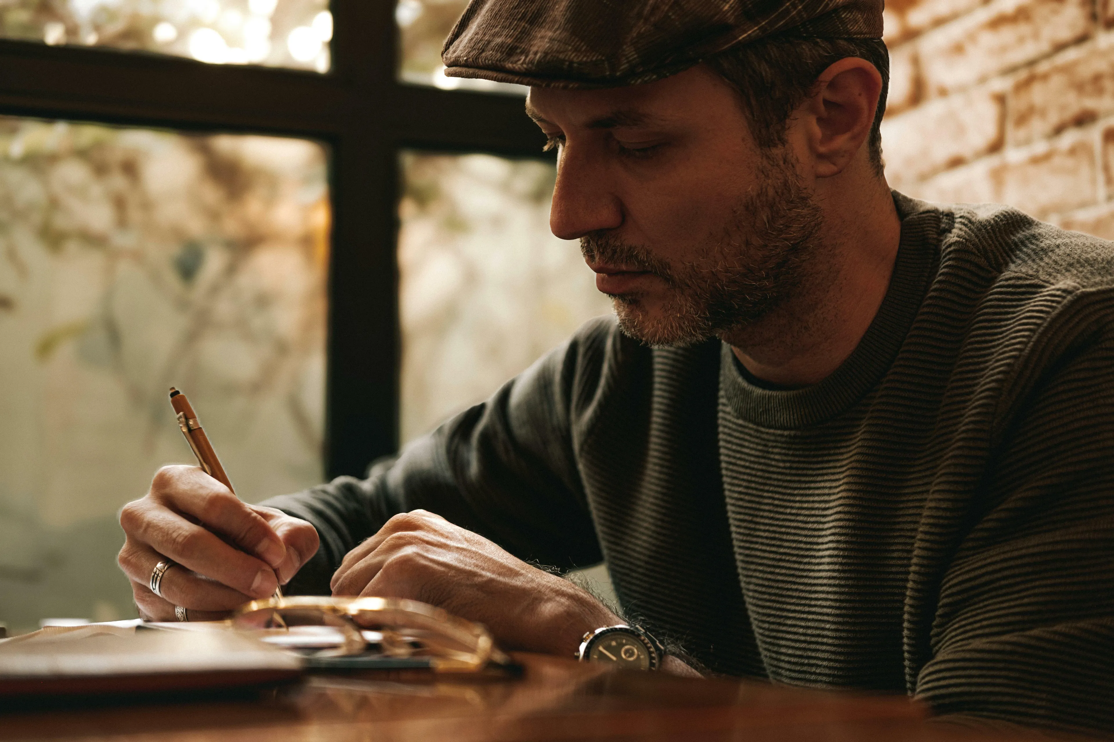 Man wearing a cap and sweater, focused on writing notes during an advanced placement school quiz on English language.