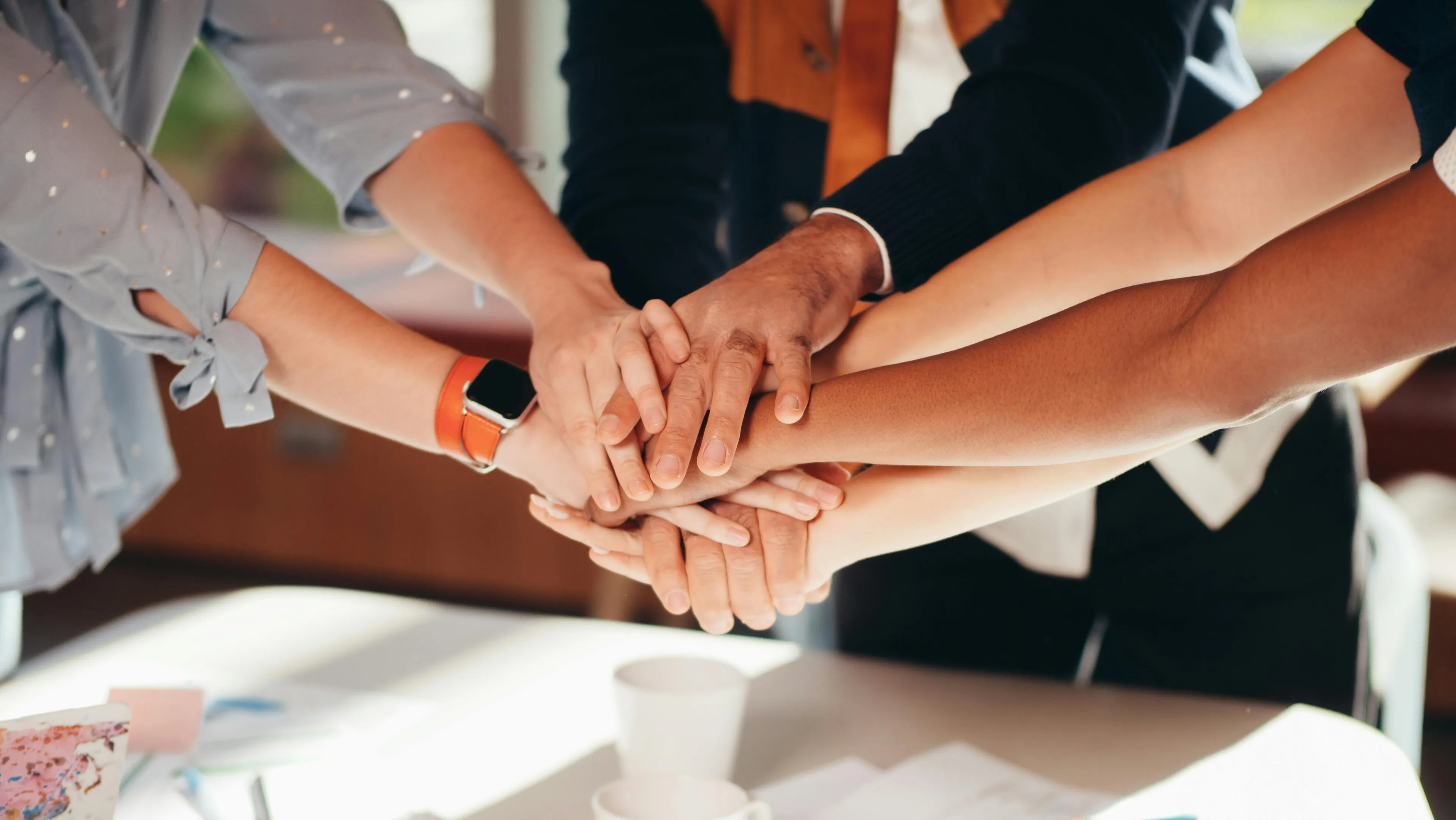 Group of diverse people joining hands in teamwork, symbolizing decision making style and collaborative support.