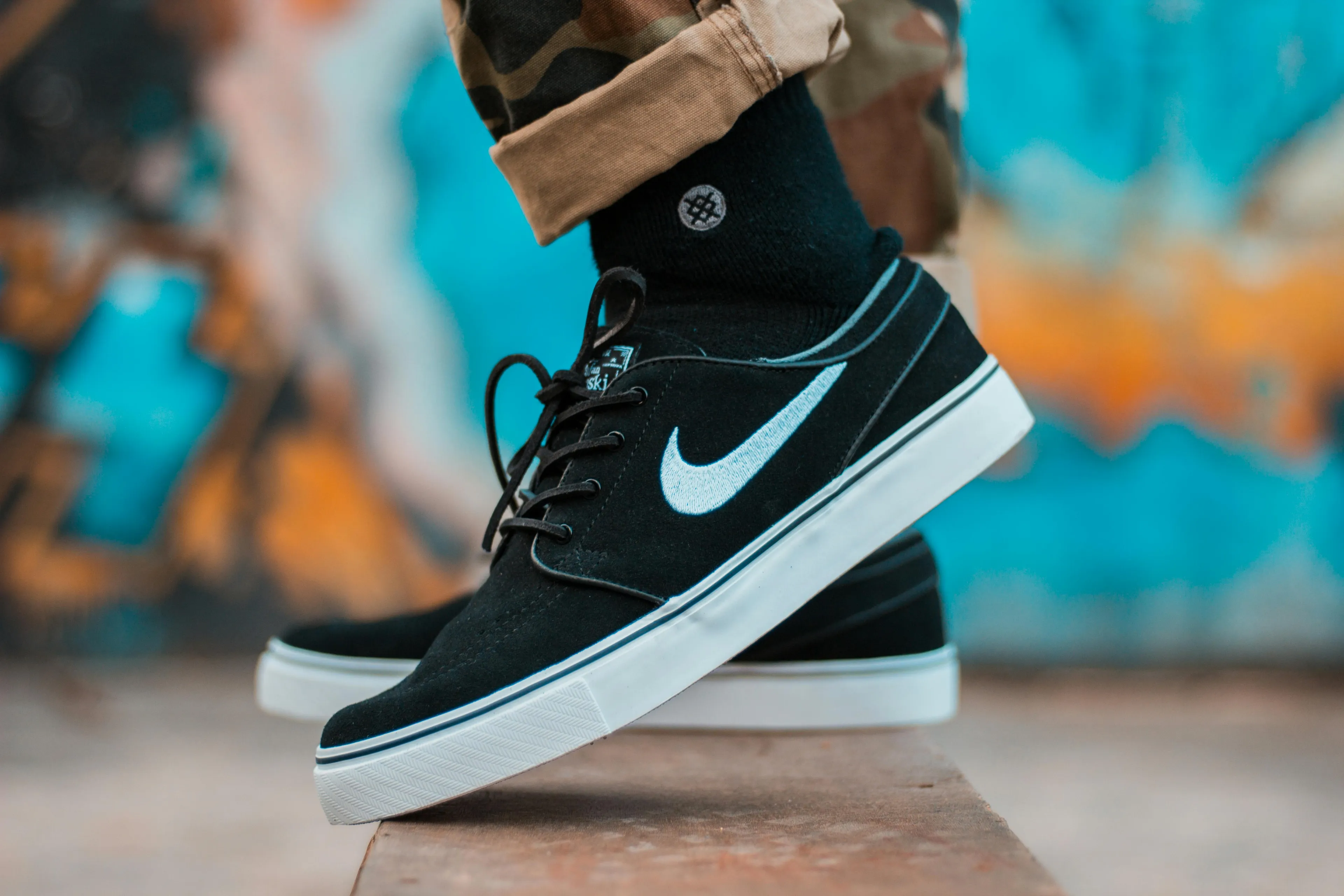 Close-up of black sneakers with white swoosh logo, worn by a person in casual pants, representing decision making style.