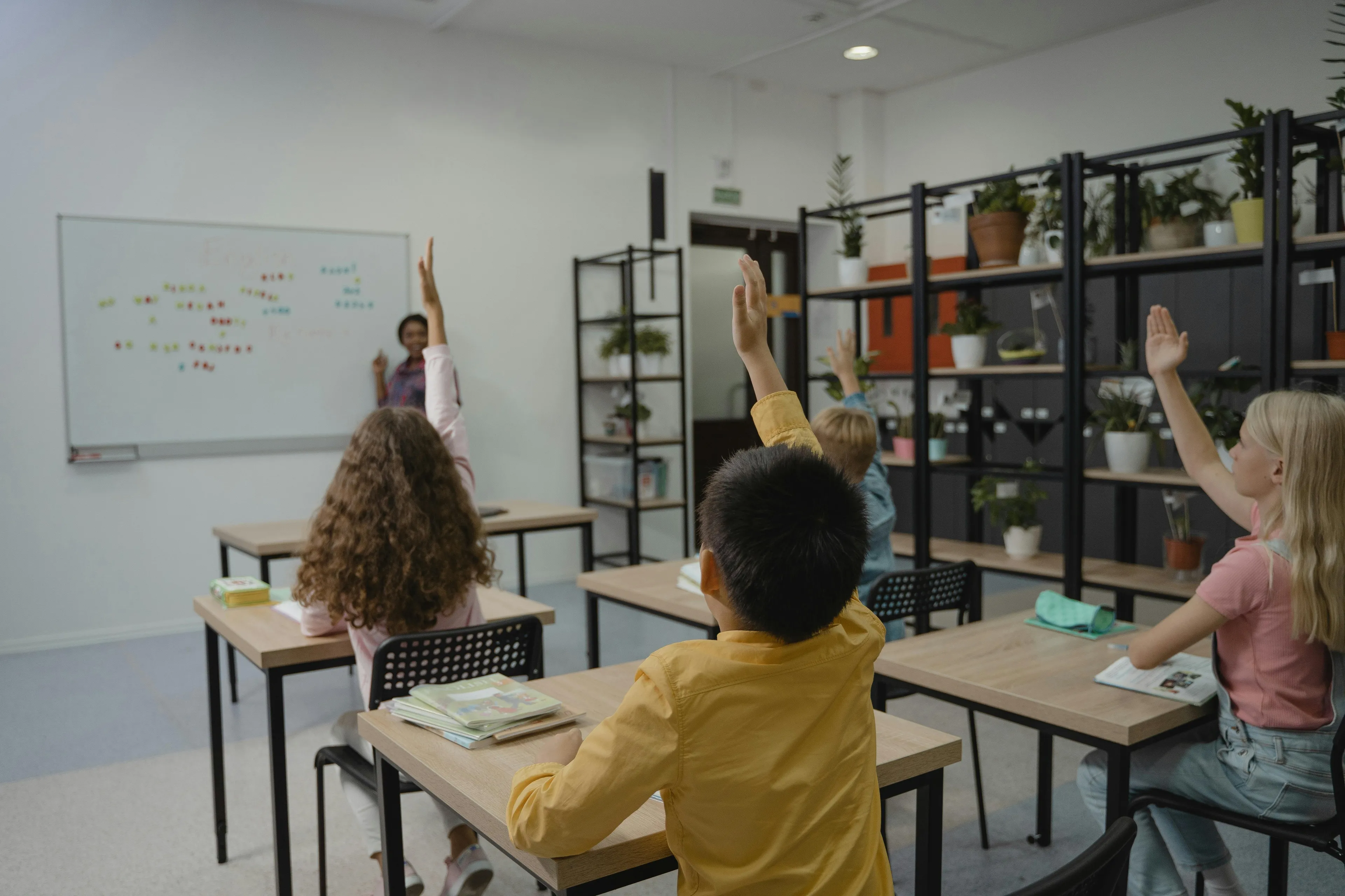 Students raising hands in a classroom participating in education programs to support charity donations.