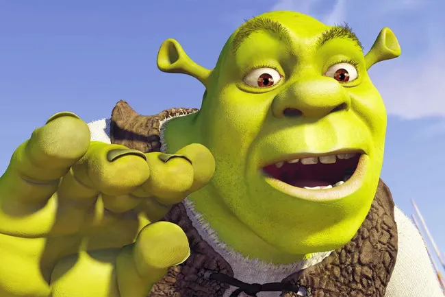 Shrek animated character in a close-up with green skin and a joyful expression reaching forward outdoors.